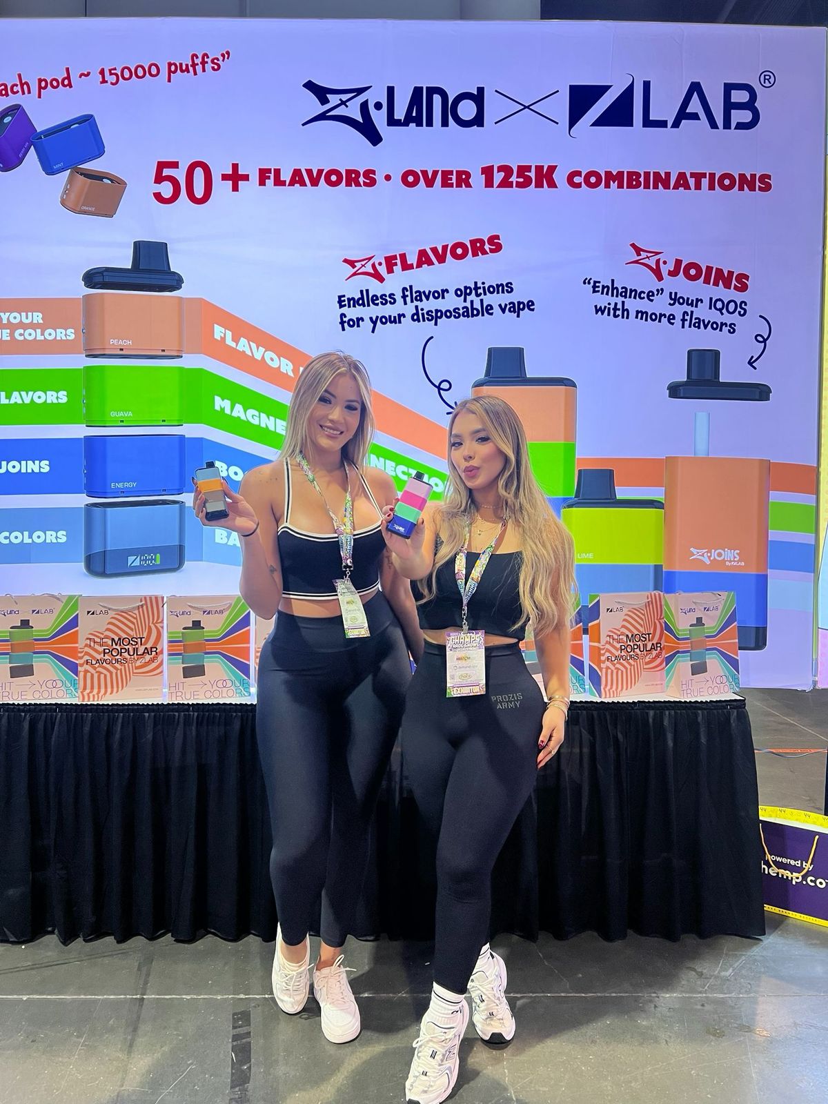 Two women holding ZLand devices in front of the ZLab booth at a trade show
